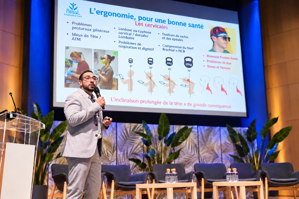 Hosam ASSAL, micro en main, explique l'effet de la posture de la tête sur les cervicales, pendant une conférence