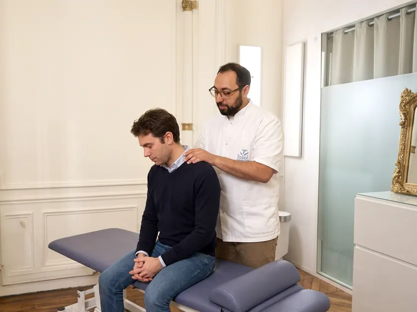 Hosam ASSAL, la main sur l'épaule d'un patient assis sur la table de soin, pendant la consultation