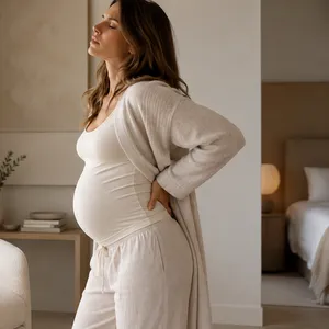 Femme enceinte debout dans sa chambre, une main sur le bas du dos