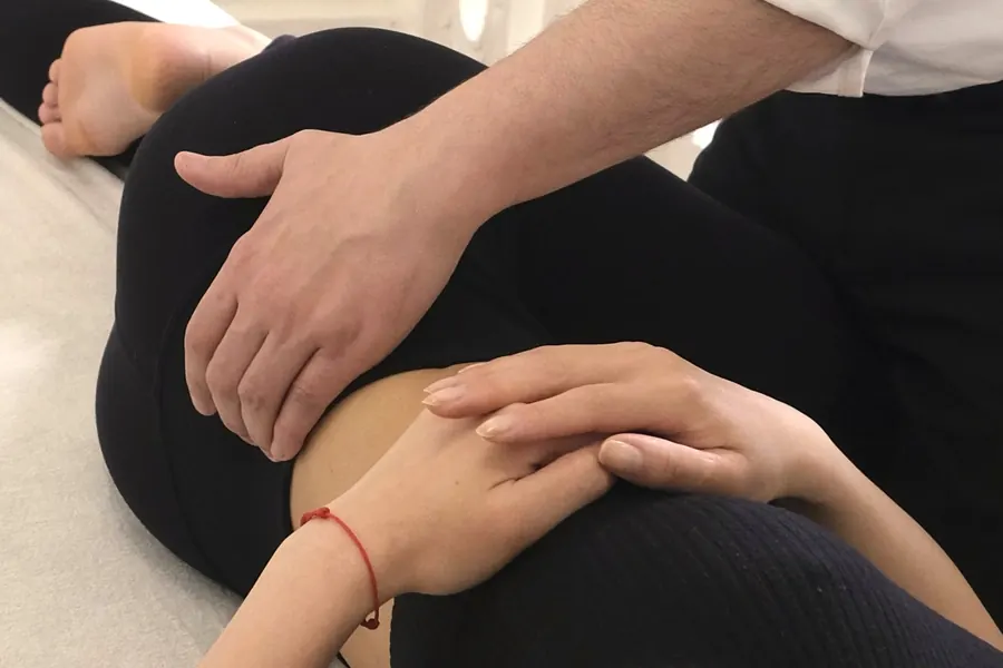 Les mains de l'ostéopathe et de la patiente posées sur le genou fléchi