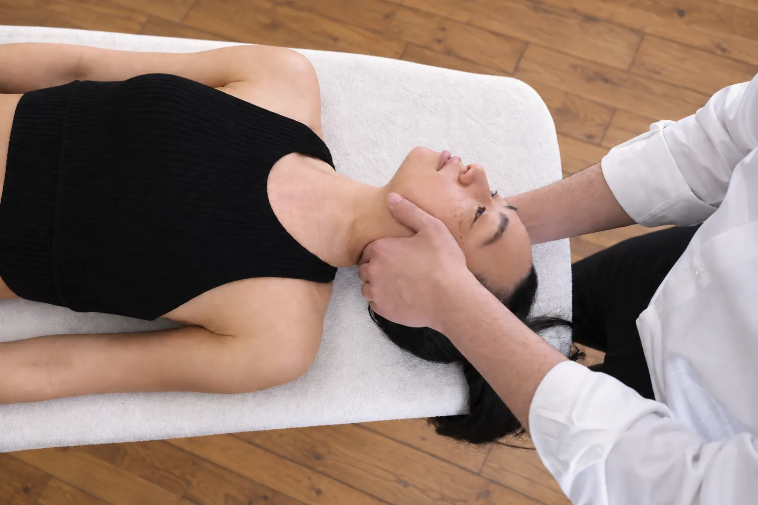 Vue de dessus : patiente allongée, la tête entre les mains de l'ostéopathe