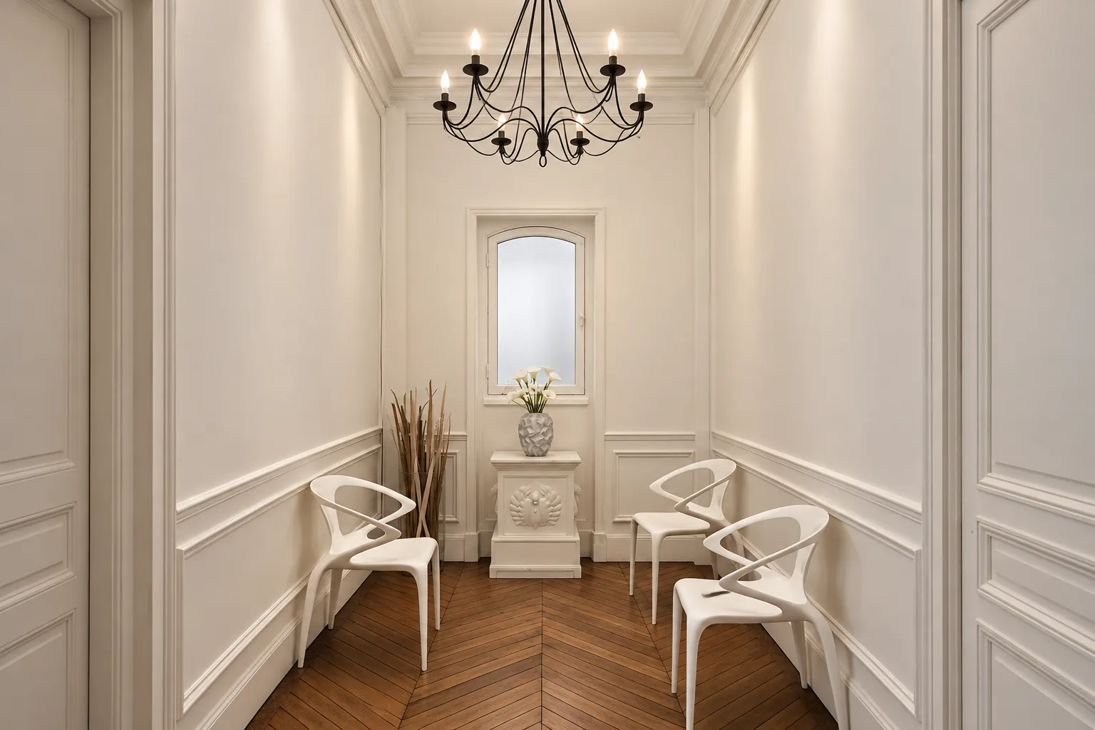 La salle d'attente du cabinet de Paris 8 : moulures, lustre, chaises blanches et parquet à chevrons
