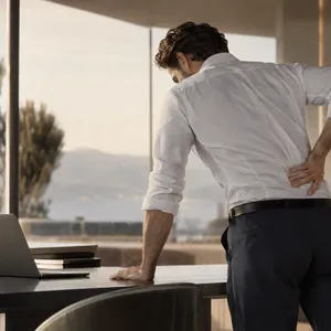 Homme penché sur un bureau, une main sur le bas du dos