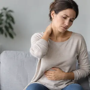 Femme sur un canapé, une main sur la nuque et l'autre sur le ventre