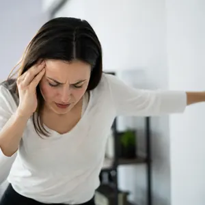 Femme prise de vertige, une main sur le front et l'autre appuyée au mur